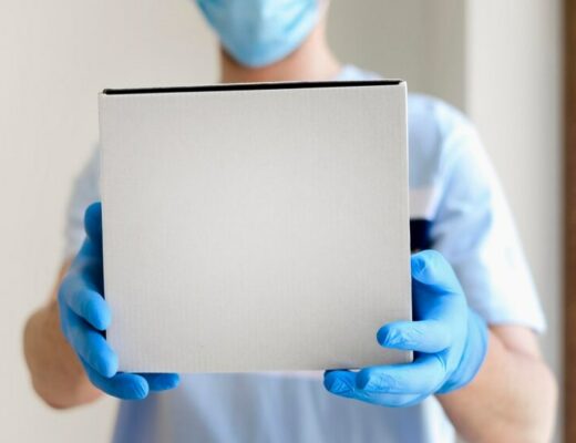 a doctor in a surgical mask and rubber gloves holding a white cardboard box